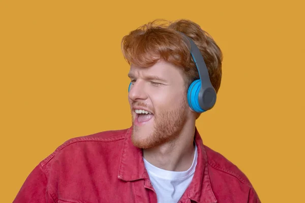Young ginger man listening to music and looking happy — Stock Photo, Image