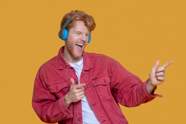 Young ginger man listening to music and feeling entertained