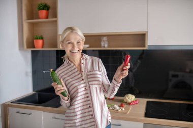 Sarışın ev hanımı elinde sebzelerle neşeli görünüyor.