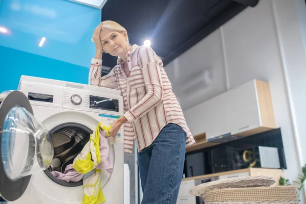 Mujer rubia de pie cerca de la lavadora un aspecto cansado —  Fotos de Stock