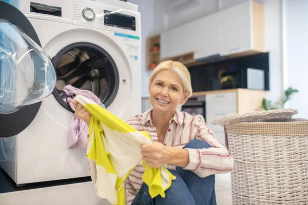 Casalinga bionda in camicia a righe e jeans seduta vicino alla lavatrice — Foto Stock