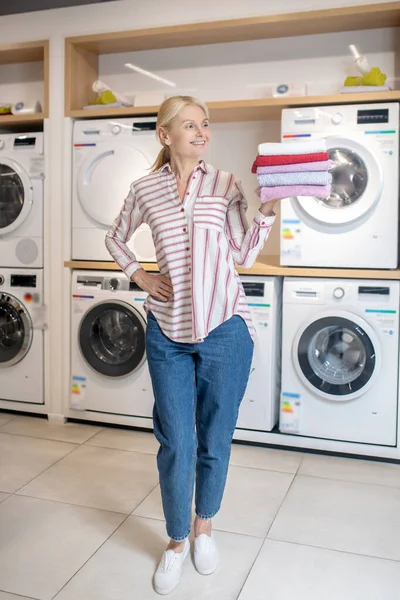 Mujer rubia sonriente de pie y sosteniendo una pila de toallas —  Fotos de Stock