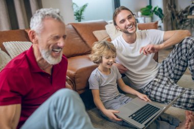 İki adam ve oğulları dizüstü bilgisayardan bir şey izliyor ve mutlu görünüyorlar.