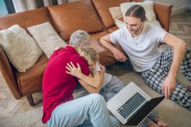 İki adam ve oğulları dizüstü bilgisayarda bir şeyler izleyip eğleniyorlar.