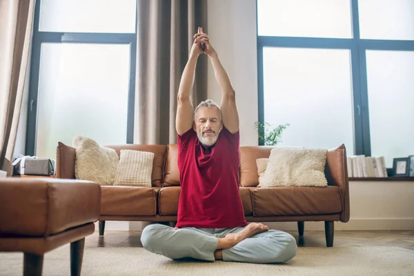 Grauhaariger Mann sitzt auf dem Boden und macht Yoga — Stockfoto