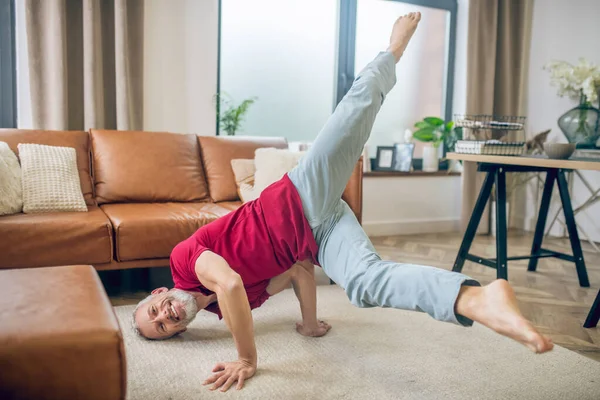 Grey-haired good-looking man doing yoga and feeling good