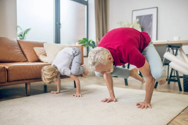 Homme en forme aux cheveux gris faisant du yoga avec son fils — Photo