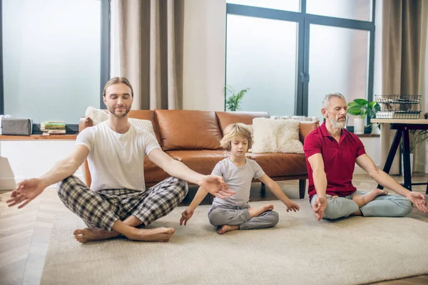 Diverse family doing yoga with kid and looking peaceful