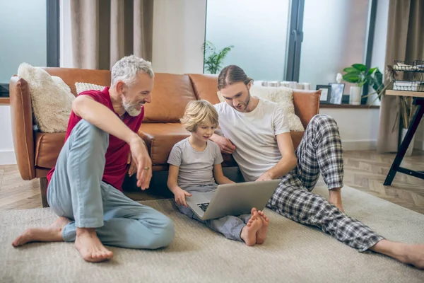 İki adam ve oğulları dizüstü bilgisayardan bir şey izliyorlar.