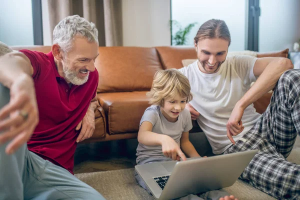 Dos hombres y su hijo viendo algo en un portátil —  Fotos de Stock