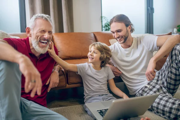 Dos hombres y su hijo viendo algo en una laptop y viéndose felices —  Fotos de Stock