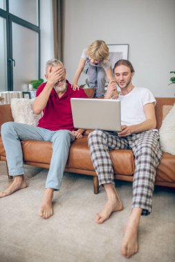 İki adam ve oğulları dizüstü bilgisayarda bir şeyler izleyip eğleniyorlar.