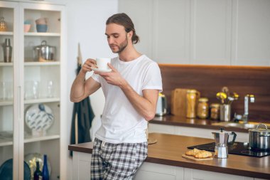 İç çamaşırlı genç mutfakta kahve içiyor.