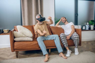 VR gözlüklü bir adam araba kullanıyor, ortağı yanında oturuyor.