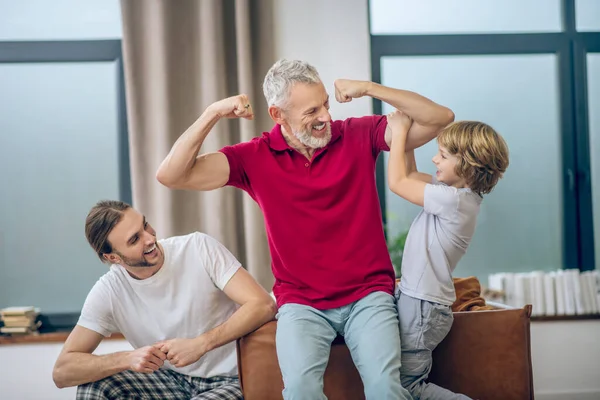 Hombre canoso mostrando sus músculos a su hijo y sintiéndose alegre —  Fotos de Stock