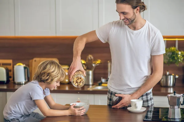 Joven en ropa de casa haciendo el desayuno para su hijo — Foto de Stock