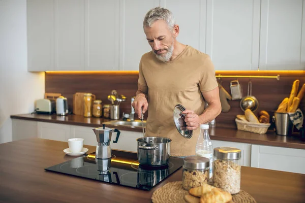 Volwassen man in beige tshirt staan in de keuken en het maken van ontbijt — Stockfoto