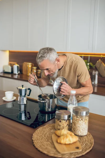 Volwassen man in beige tshirt koken in de keuken — Stockfoto