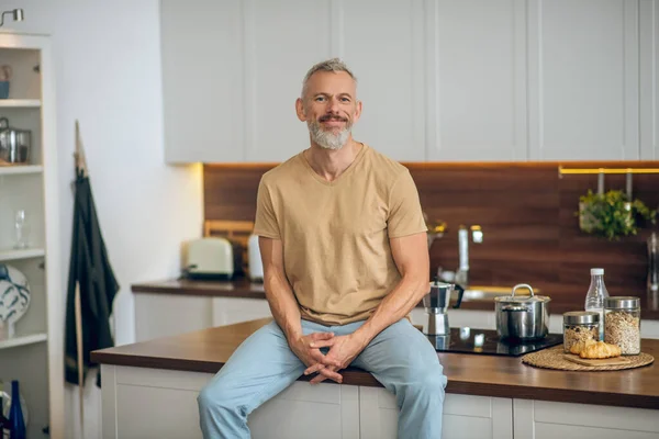 Зрелый мужчина в бежевой футболке на кухне дома — стоковое фото