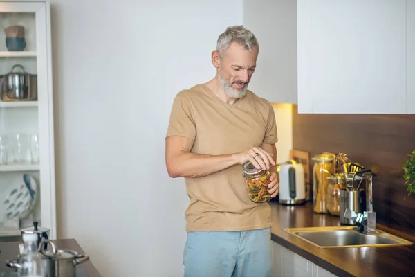 Volwassen man met baard in beige tshirt in de keuken thuis — Stockfoto