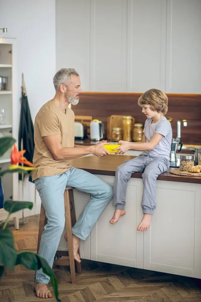 Volwassen man in beige tshirt en zijn zoon in de keuken thuis — Stockfoto