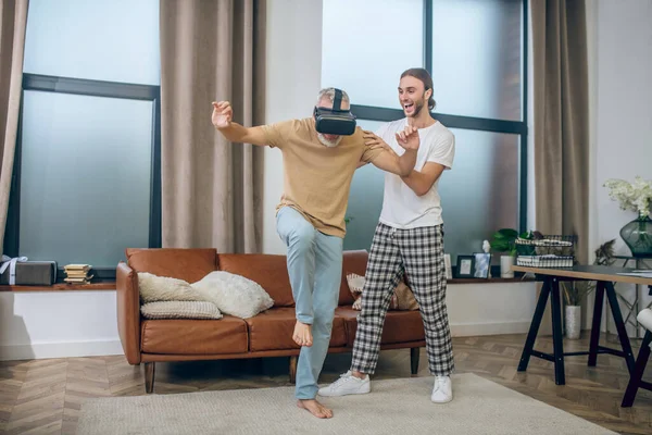 Hombre en gafas vr caminando en la habitación, su compañero apoyándolo — Foto de Stock