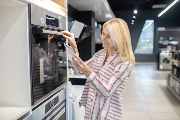 Rubia cliente buscando involucrado al elegir el horno en una sala de exposición — Foto de Stock