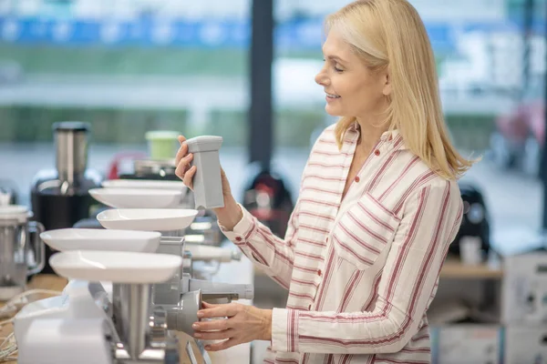 Blonde Frau steht in einem Verkaufsraum für Konsumgüter und wählt eine Hackmaschine — Stockfoto