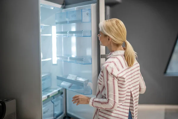 Blonde female customer choosing a fridge in a megastore — Stock Photo, Image