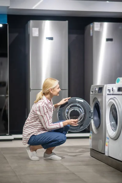 Çizgili gömlekli bir kadın galeride çamaşır makinesini seçiyor ve ilgileniyor görünüyor. — Stok fotoğraf
