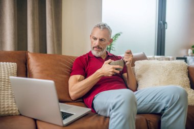 Grey-haired man having lunch and watching a video clipart