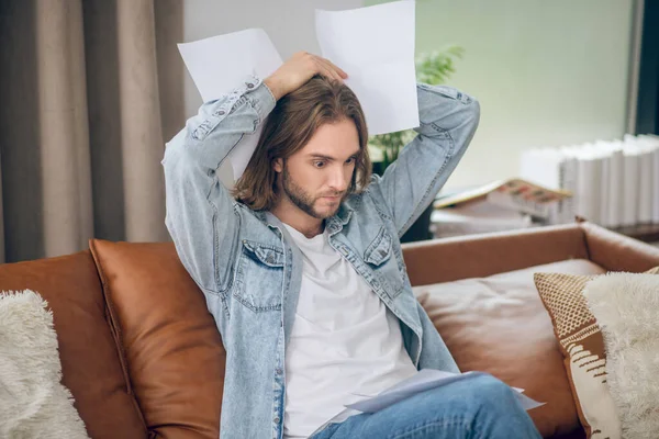 Hombre joven en jeans camisa sosteniendo papeles y mirando estresado — Foto de Stock
