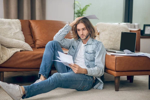 Ung man i jeans skjorta håller papper och ser stressad ut — Stockfoto