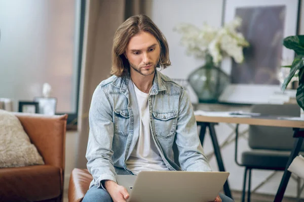 Man in jeans shirt werkt op laptop en ziet er verward uit — Stockfoto