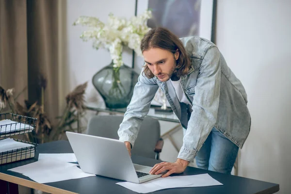 Man in jeans shirt werkt aan laptop en ziet er druk uit — Stockfoto