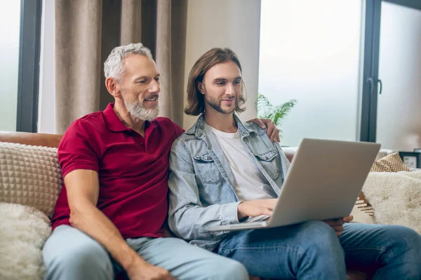 Dos hombres sentados uno al lado del otro y viendo algo en el portátil — Foto de Stock