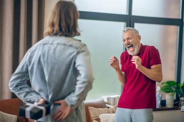 Hombre de pelo gris que parece feliz recibiendo un regalo de su pareja — Foto de Stock