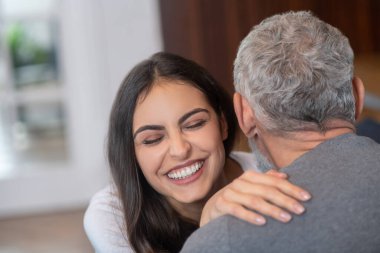 Genç, uzun saçlı, gri saçlı eşine sarılan bir kadın.