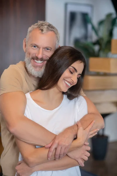 Бородатый мужчина и молодая женщина обнимаются и выглядят счастливыми — стоковое фото