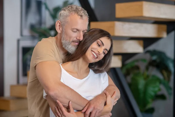 Barbudo hombre y mujer joven abrazando y mirando feliz —  Fotos de Stock