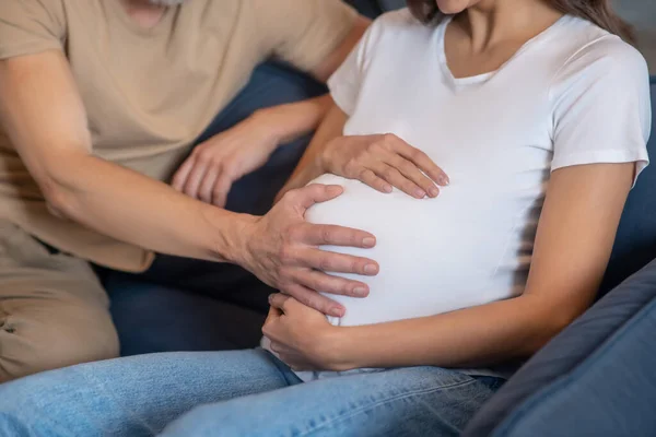 Щасливий зрілий чоловік торкається живота своєї молодої вагітної дружини — стокове фото
