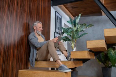 Gri saçlı, olgun, kendine güvenen bir adam evde çalışıyor.