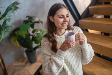 Genç, siyah saçlı, güzel bir kadın kahve içiyor ve gülümsüyor.