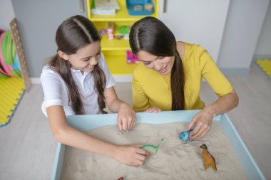 Gülümseyen kadın ve kız kumdaki figürleri yeniden düzenliyor.