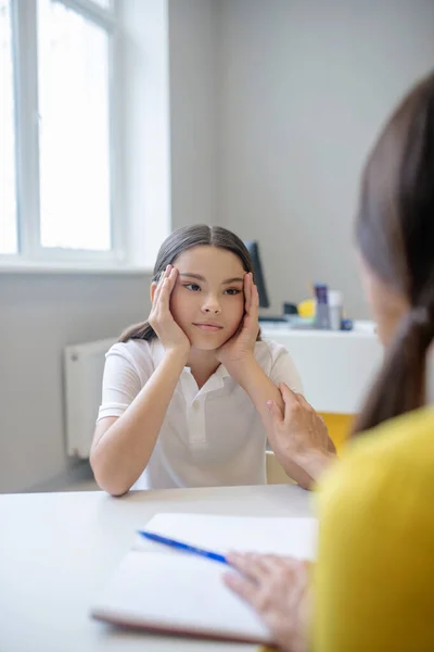 Ragazza seria che si tiene per mano vicino al viso e psicologo — Foto Stock