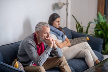 Karısının yanındaki koltukta oturan düşünceli bir adam.