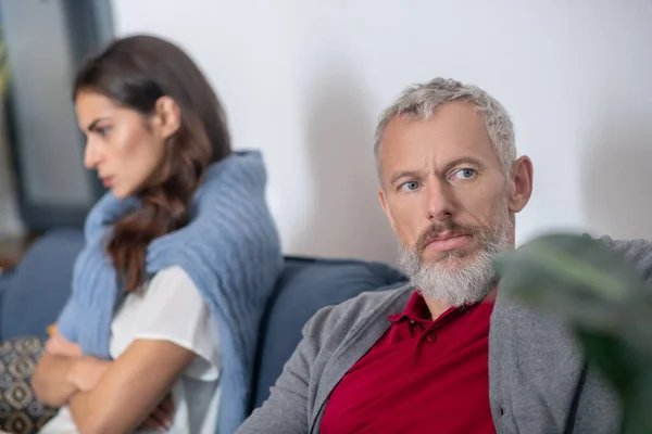 Разочарованный бородатый мужчина сидит рядом со своей женой — стоковое фото