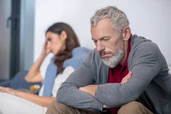 Upprörd skäggig man sitter nära sin fru efter ett gräl — Stockfoto