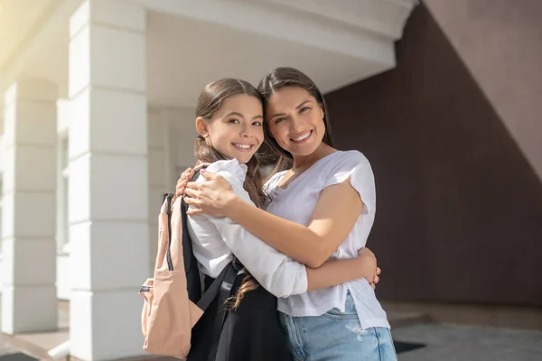 Mamá e hija abrazadas de pie cerca de la escuela —  Fotos de Stock