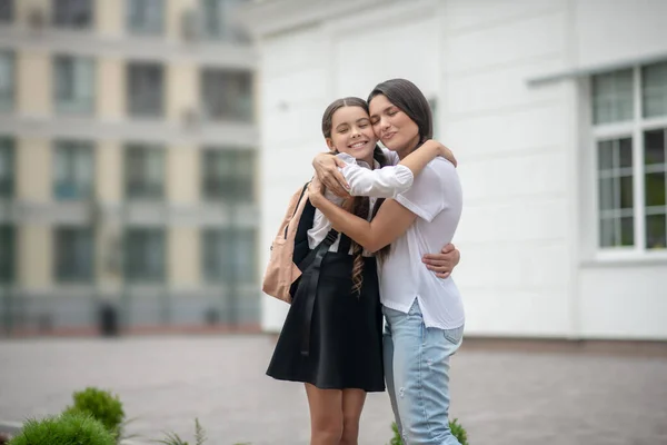 Feliz mamá y su hija abrazados en el patio de la escuela —  Fotos de Stock